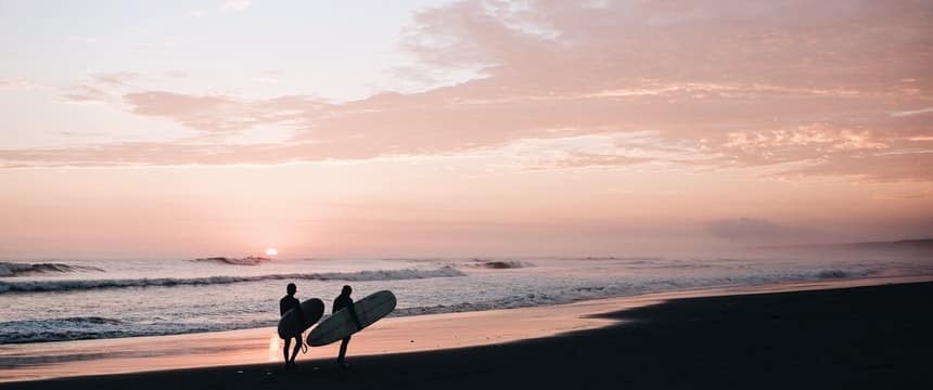 Two surfers walking to the sea at sunset