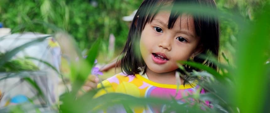 Child standing among tall green garden plants